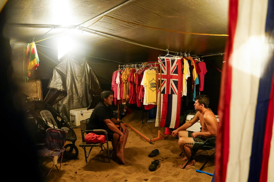 Blake Ramelb, left, talks with De Andre Makakoa, right, in Makakoa's tent at a housing protest on Kaanapali Beach Wednesday, Dec. 6, 2023, in Lahaina, Hawaii. A group of survivors is camping on the resort beach to protest and raise awareness for better long-term housing options for those displaced. Residents and survivors still dealing with the aftermath of the August wildfires in Lahaina have mixed feelings as tourists begin to return to the west side of Maui, staying in hotels still housing some displaced residents. (AP Photo/Lindsey Wasson)