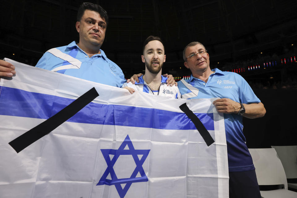Black mourning bands are seen on the Israeli flag as Israel's Artem Dolgopyat and his coaches celebrate winning the gold medal on the floor exercise during the apparatus finals at the Artistic Gymnastics World Championships in Antwerp, Belgium, Saturday, Oct. 7, 2023. (AP Photo/Geert vanden Wijngaert)