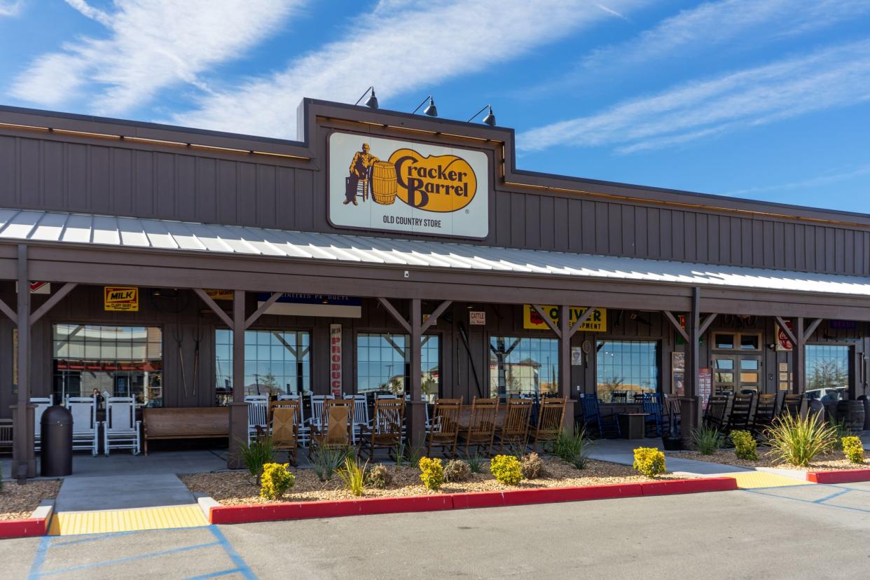 Front exterior porch area and door of Cracker Barrel restaurant in Victorville, California with a two rows of rocking chairs facing each other and garden area with parking in the foreground and bright blue sky in the background