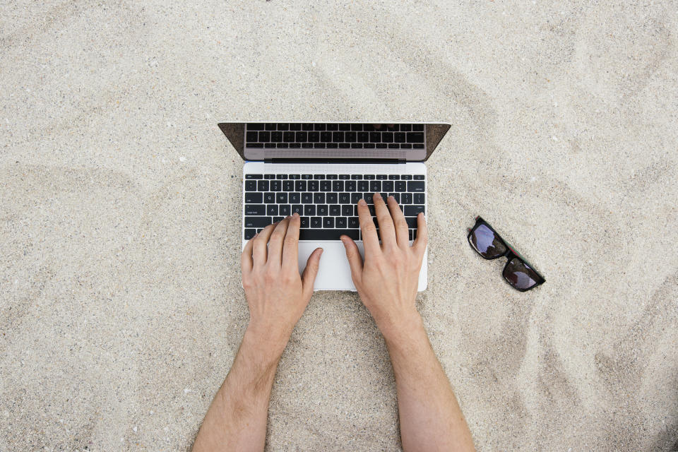 Man hands using laptop with sunglasses near it on a sandy beach, shot directly from above in South Beach, Miami, Florida, USA.