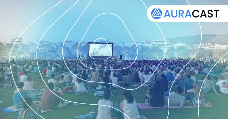 Bluetooth Auracast being used at a festival, on a big screen with people watching and listening