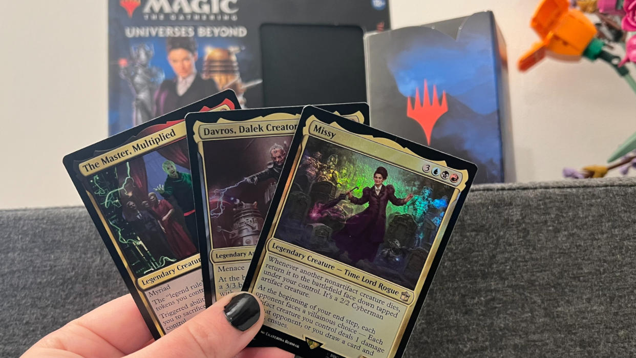  Three cards from Magic: The Gathering Doctor Who being held up in front of the Commander Deck box. 