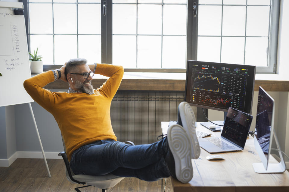 Mature businessman and experienced investor leans back in his chair while looking at multiple monitors with various stock charts and graphs