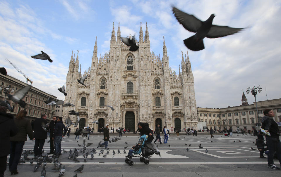 This Jan. 16, 2014 photo shows visitors dodging birds in the piazza outside of Duomo cathedral in Milan, Italy. The ornate white facade of Milan's Duomo cathedral is the single most recognized symbol of the Lombard capital, taking centuries to complete. (AP Photo/Antonio Calanni)