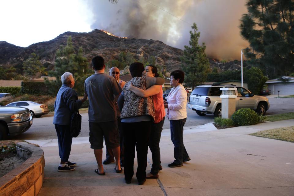 Family members comfort each other as they evacuate their home as firefighters battle a wildfire, Thursday, Jan. 16, 2014, in Azusa, Calif. A wildfire burned out of control near homes in the dangerously dry foothills of the San Gabriel Mountains early Thursday, fanned by gusty Santa Ana winds that spit embers into neighborhoods in the city below, igniting trees. Evacuations were ordered for houses at the edge of the fire. (AP Photo/Jae C. Hong)