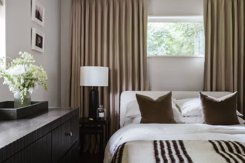 White linens on bed, black and white striped throw blanket, beige curtains, black modern dresser