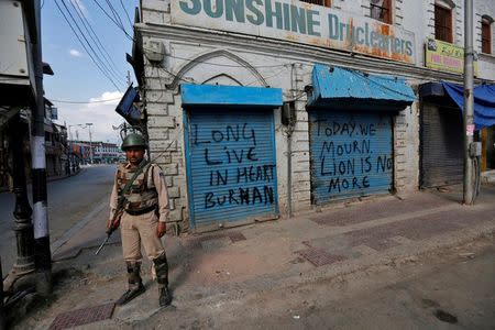 An Indian policeman stands guard in front of closed shops painted with graffiti during a curfew in Srinagar July 12, 2016. REUTERS/Danish Ismail