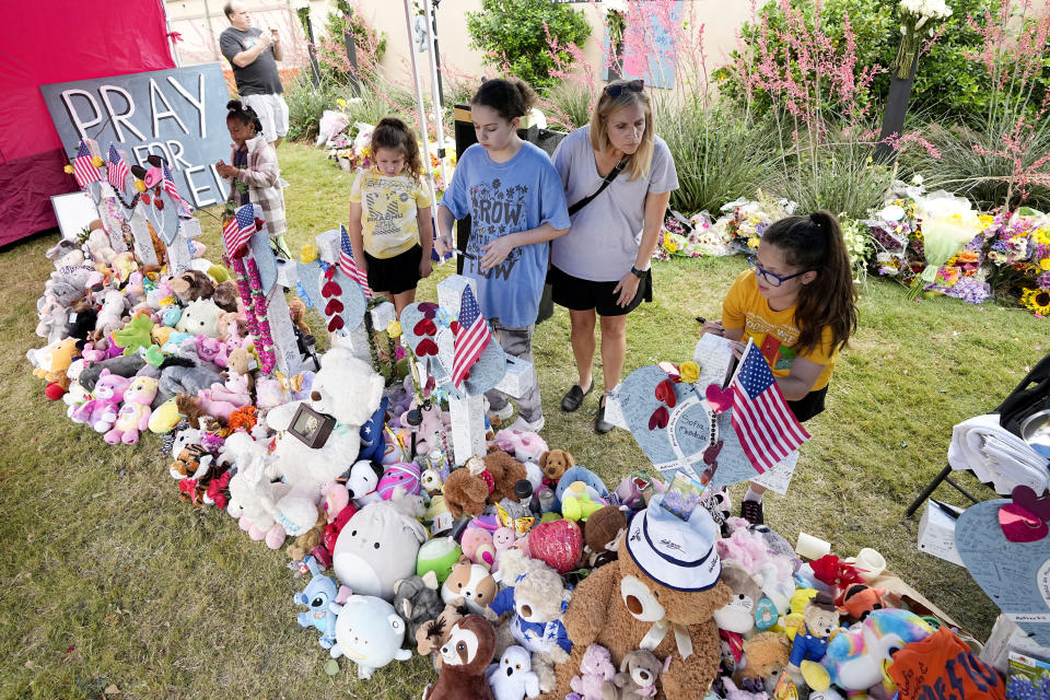 Sarah Mandell, of Allen, Texas, second from right, stands by her daughters Callie, second from left, Libby and Mattie, right, as they leave messages on crosses at a makeshift memorial, Wednesday, May 10, 2023, in Allen, Texas, by the mall where several people were killed. (AP Photo/Tony Gutierrez)