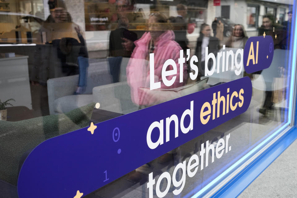 People reflected in a window of a building at the Davos Promenade with a slogan about AI alongside the World Economic Forum in Davos, Switzerland, Thursday, Jan. 18, 2024. The AI technology has taken a large and growing slice of attention in Davos, this year the theme of Artificial Intelligence "as a driving force for the economy and society" will get about 30 separate sessions. (AP Photo/Markus Schreiber)