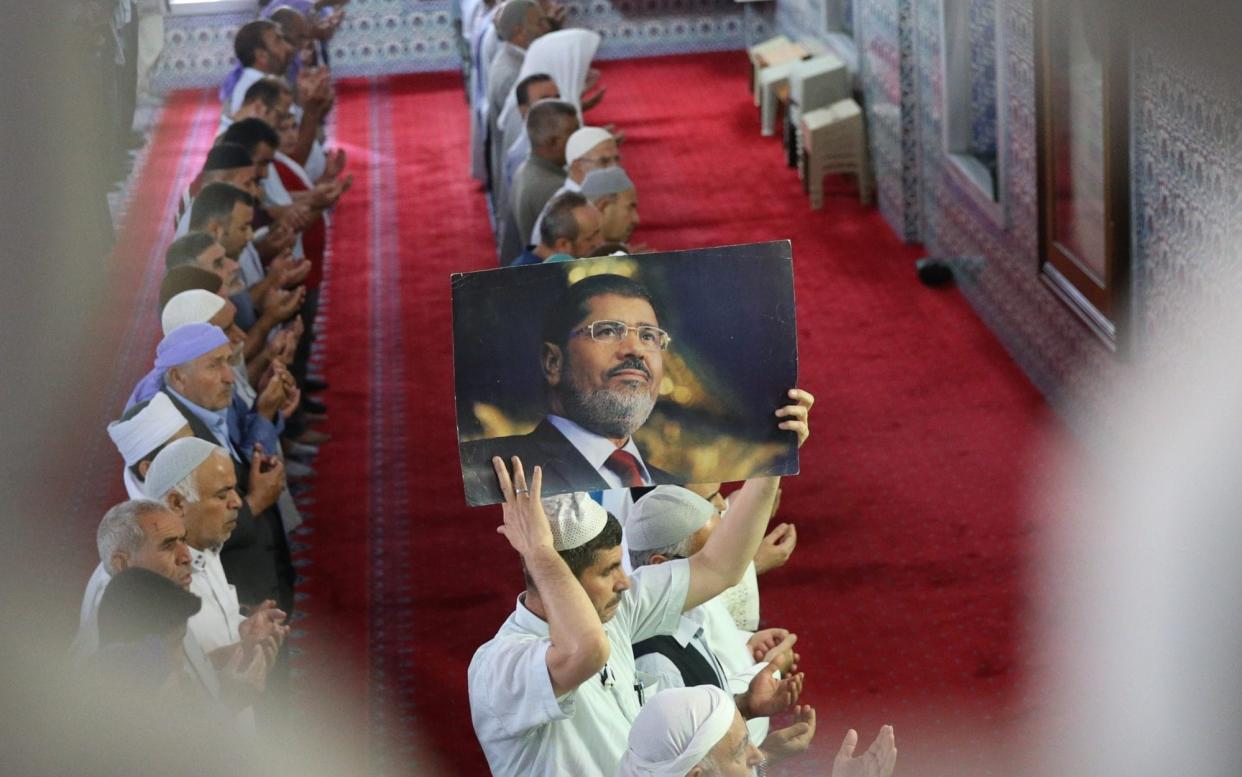 A man holds up an image of former Egyptian President Mohamed Morsi during a funeral prayer in absentia - Anadolu