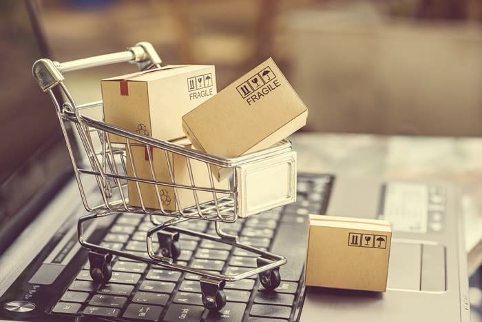 A mini shopping cart full of boxes sitting on a laptop keyboard, illustrating e-commerce.