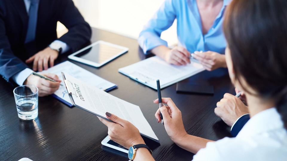 Unrecognizable business partners discussing agreement conditions reviewing it together at meeting.