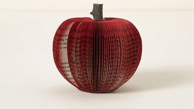 a red paper apple made from book pages with a wooden stem from a tree