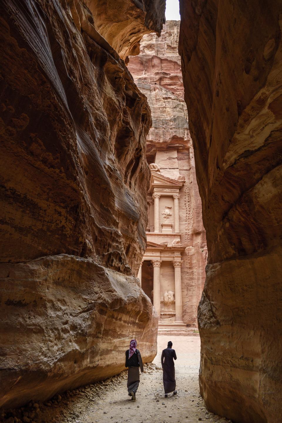 <h1 class="title">Two people walking through narrow rock formation towards rock-cut architecture of Al Khazneh or The Treasury at Petra, Jordan.</h1><cite class="credit">Photo: Mint Images / Getty Images</cite>