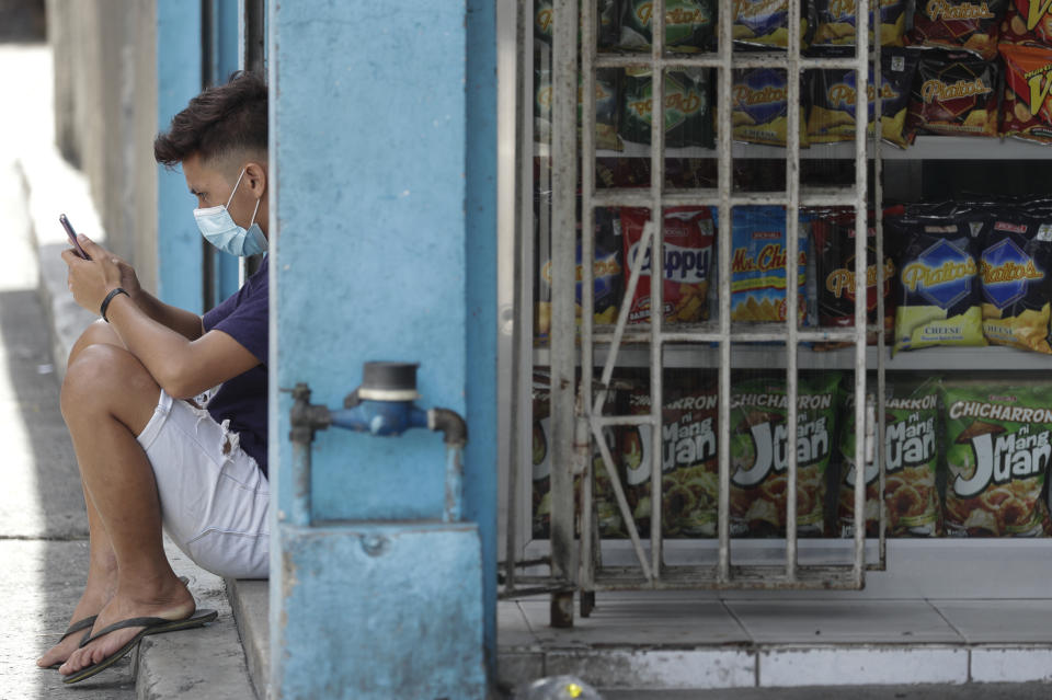 A man wearing a mask uses his smartphone outside a store in Manila, Philippines on Monday, Aug. 3, 2020. Philippine President Rodrigo Duterte is reimposing a moderate lockdown in the capital and outlying provinces after medical groups appealed for the move as coronavirus infections surge alarmingly. (AP Photo/Aaron Favila)