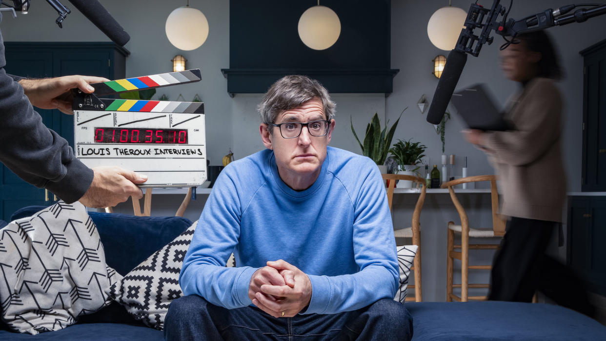 Louis Theroux sits on a blue sofa