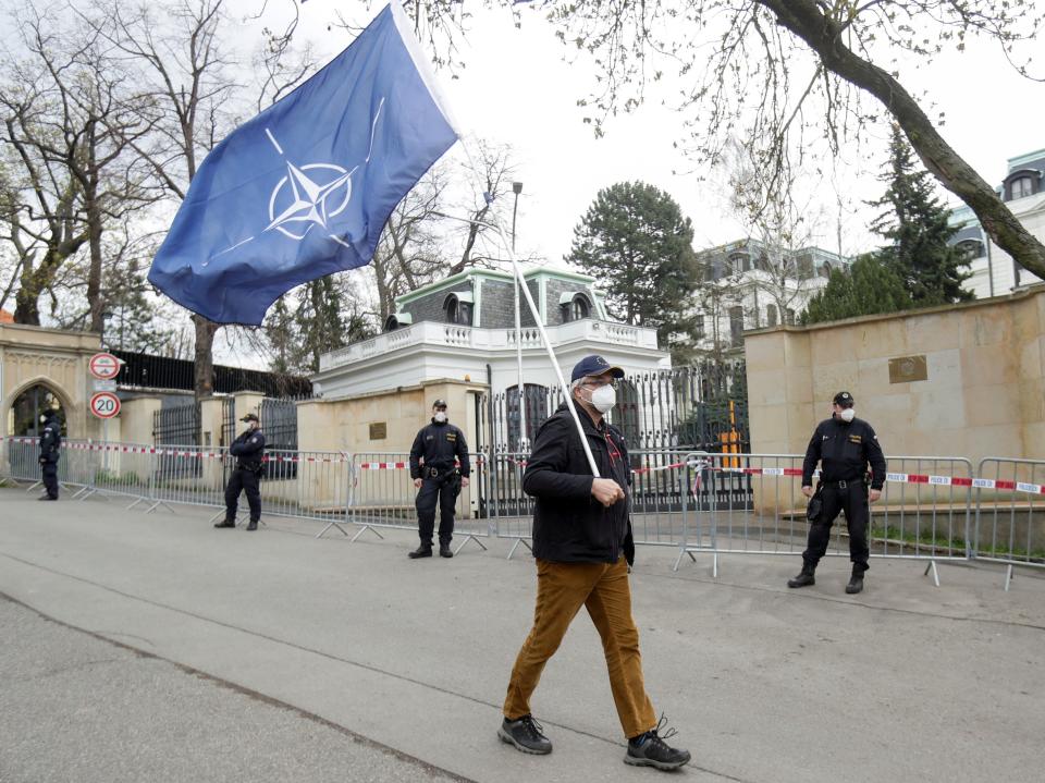 A man carrying a Nato flag to protest over Russian intelligence services’ alleged involvement in an ammunition depot explosion in the Vrbetice area in 2014 walks past police officers outside the Russian embassy in Prague, 18 April 2021David W Cerny/Reuters