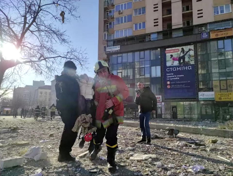 Emergency service workers carrying a person at the site of a damaged multi-storey residential building.