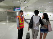 A SBS Transit "goodwill ambassador" advises a couple on their journey route in front of the North East Line section at Dhoby Ghaut station. (Yahoo! photo/Jeanette Tan)