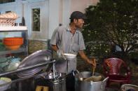 Pham Van Sang, a 50-year-old street food vendor who migrated from the Mekong Delta, shares a light moment with a customer while preparing a noodle dish in Ho Chi Minh City, Vietnam, Monday, Jan. 22, 2024. He sells noodles in the city's industrial zone, a destination for many migrants from the Mekong Delta seeking a better life as he did. (AP Photo/Jae C. Hong)