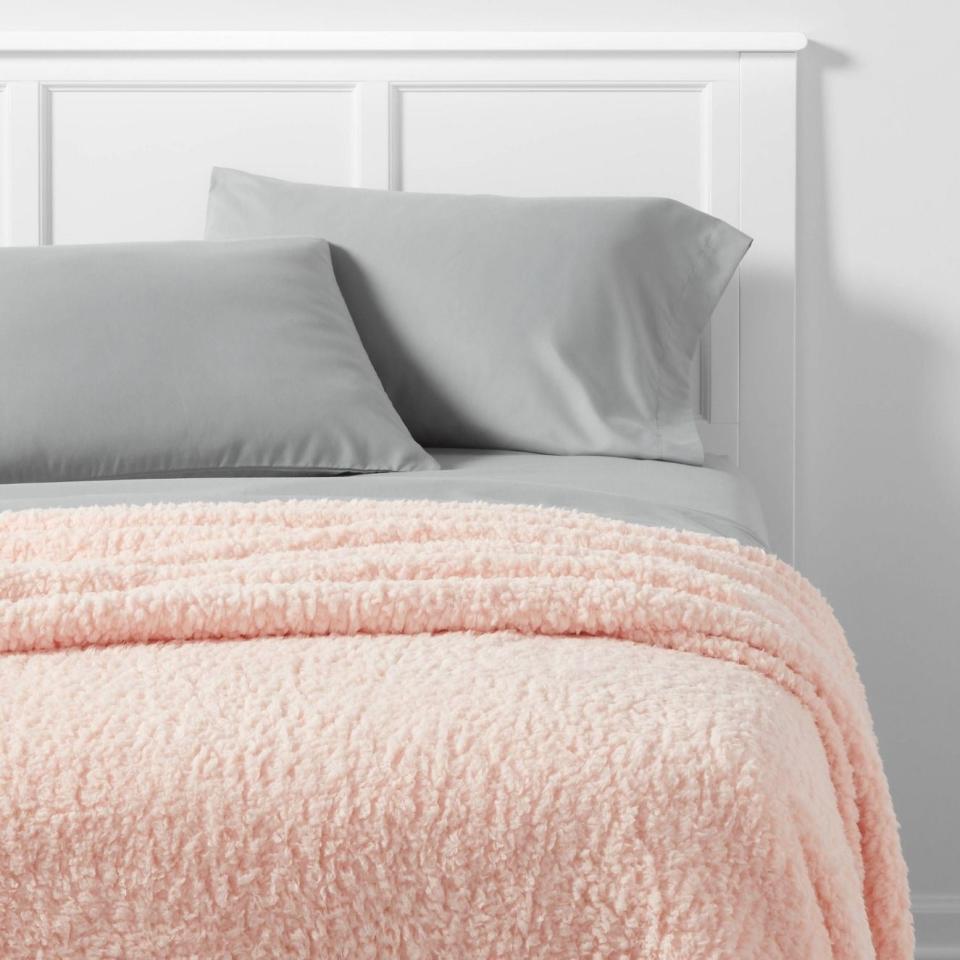 Bed with a white headboard, gray pillow, and plush pink blanket