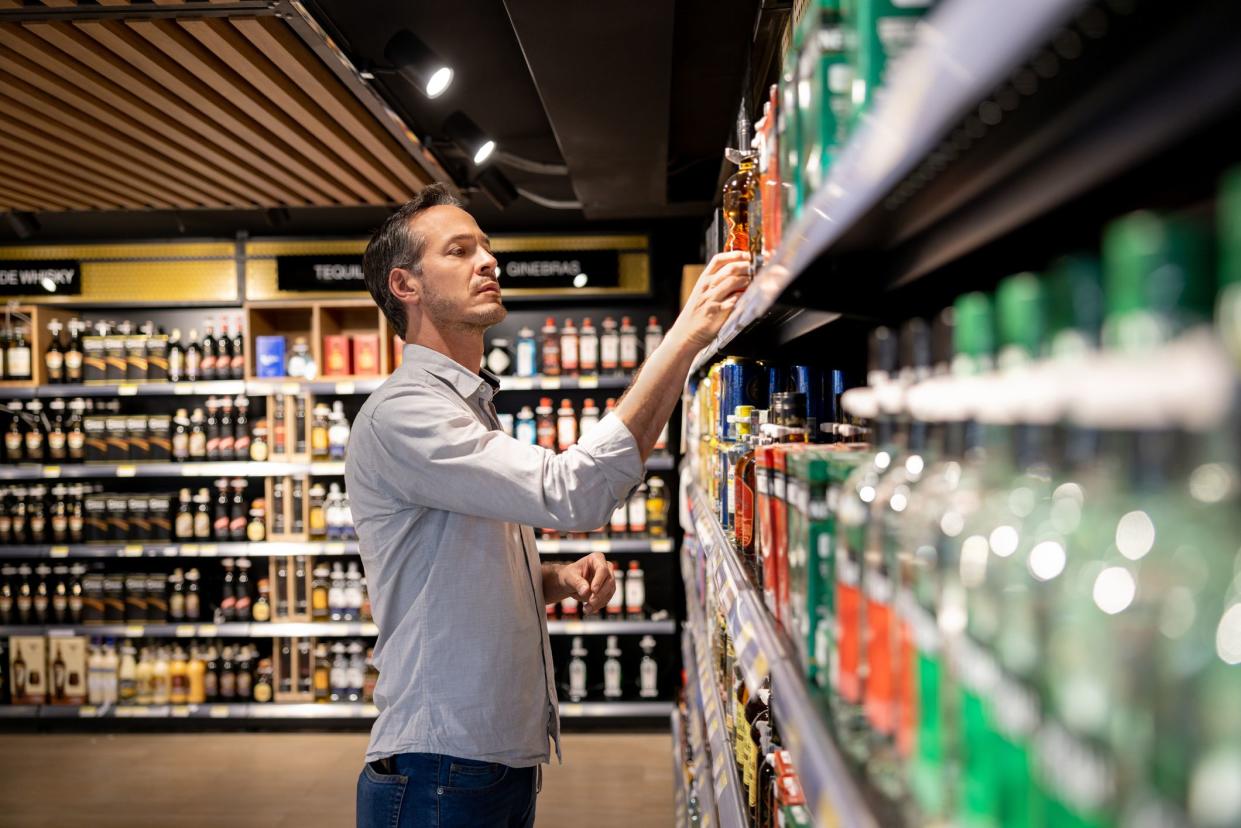 Latin American man at the supermarket buying a bottle of alcohol - grocery shopping concepts
