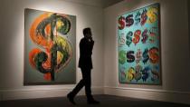 A visitor talks on the phone as he walks past "Dollar Sign" (L) and "Dollar Signs" by Andy Warhol at Sotheby's in London, Britain June 19, 2015. REUTERS/Suzanne Plunkett