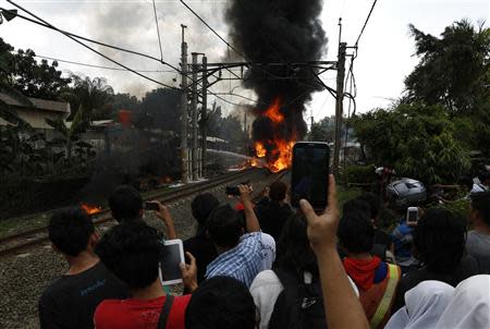 People take pictures of a burning commuter train after it collided at Bintaro district in Jakarta, December 9, 2013. Seven passengers died and at least 20 injured after a commuter train collided with a truck loaded with gasoline in south Jakarta, according to a police spokesman. REUTERS/Beawiharta