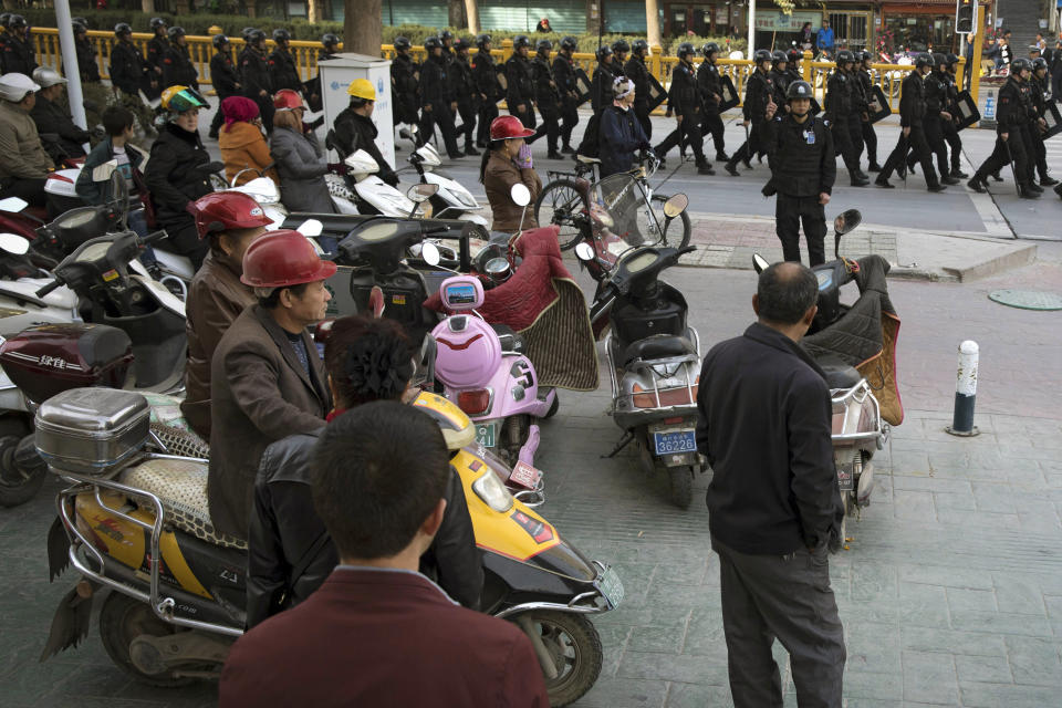 FILE - In this Nov. 5, 2017, file photo, residents watch a convoy of security personnel armed with batons and shields patrol through central Kashgar in western China's Xinjiang region. China says on Monday, March 18, 2019 it has arrested nearly 13,000 people it describes as terrorists in the traditionally Islamic region of Xinjiang since 2014 and broken up hundreds of "terrorist gangs." The figures were included in a government report on the situation in the restive northwestern territory that seeks to respond to growing criticism over the internment of an estimated 1 million members of the Uighur (WEE-gur) and other predominantly Muslim ethnic groups. (AP Photo/Ng Han Guan, File)