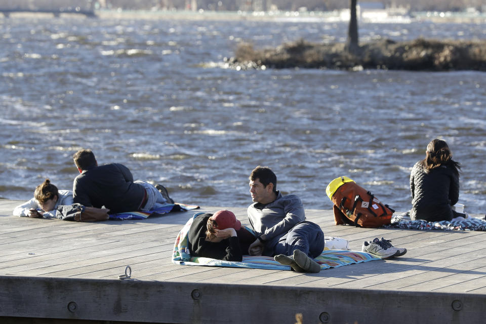 Phil Taneyhill, center right, and his wife Elisa, center left, both of Boston, sit on a dock in the Charles River Esplanade park, in Boston, Sunday, Jan. 12, 2020, while enjoying unseasonably warm weather. Temperatures climbed into the low 70s in many places in the state Sunday. (AP Photo/Steven Senne)