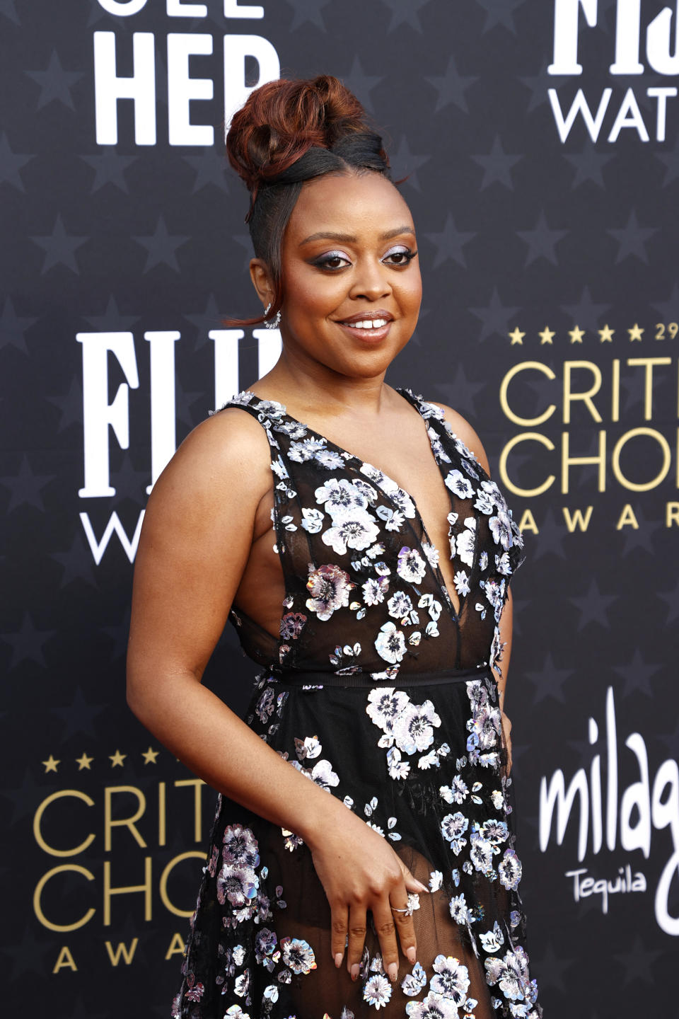 Person posing on red carpet, wearing a floral dress with a plunging neckline and updo hairstyle