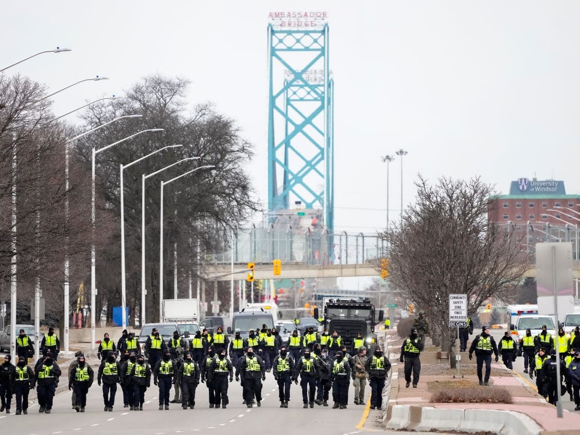 Police walk the line to remove protesters on Sunday morning near the Ambassador Bridge in Windsor, Ont. Officers from multiple police forces advanced to clear out the remaining protesters and break up a days-long blockade of truckers and others opposed to COVID-19 health measures, including vaccine mandates. (Nathan Denette/The Canadian Press - image credit)