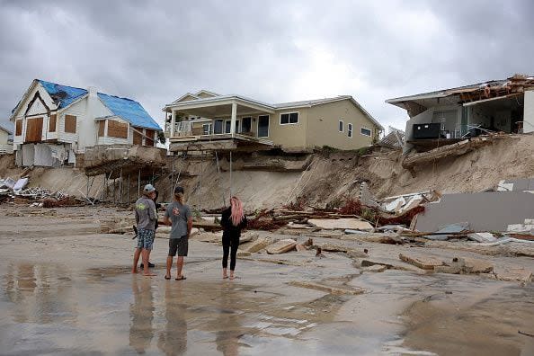 People look on at homes that are partially toppled onto the beach after Hurricane Nicole came ashore on November 10, 2022, in Daytona Beach, Florida. Nicole came ashore as a Category 1 hurricane before weakening to a tropical storm as it moved across the state.