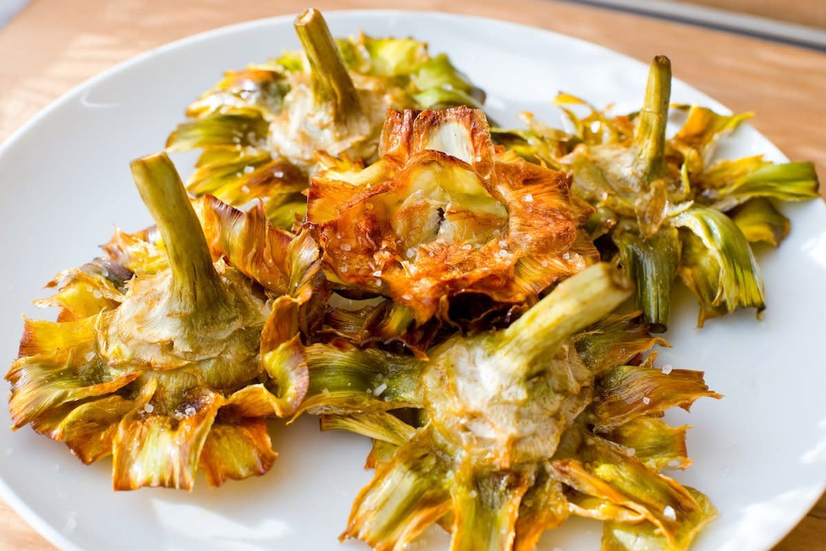 Roman fried artichokes (Jewish style) with flakes of sea salt on a wooden table.