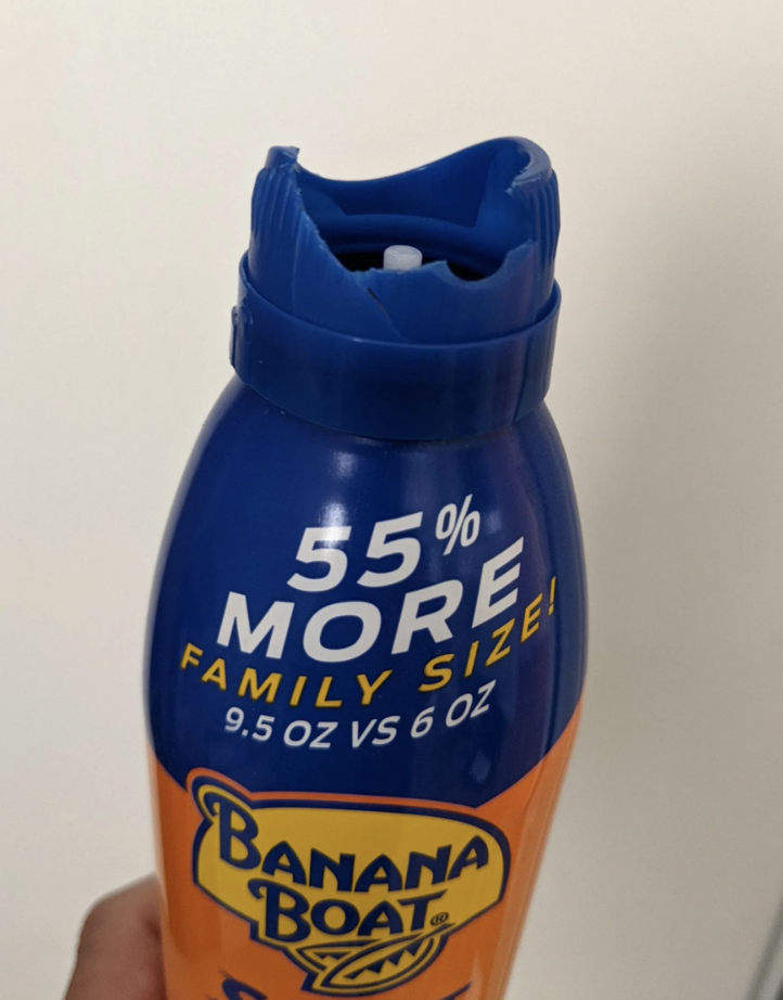 A hand holding a Banana Boat sunscreen bottle with the top and spray nozzle broken
