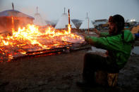 <p>An opponent of the Dakota Access oil pipeline warms his hands beside a building set on fire by protesters preparing to evacuate the main opposition camp fighting the pipeline, near Cannon Ball, N.D., Feb. 22, 2017. (Photo: Terray Sylvester/Reuters) </p>