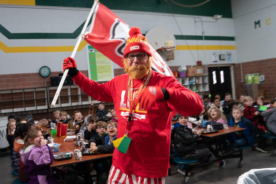 Dressed as Kansas City Chiefs tight end Travis Kelce, Vic Williams, principal of McEachron Elementary School, waves a Chiefs flag as he enters his school's cafeteria Tuesday to rally students at lunch time.