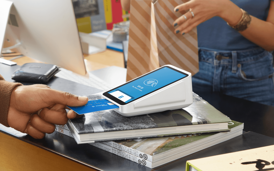 A merchant inserting a credit card into a Square payment terminal with a customer standing by.