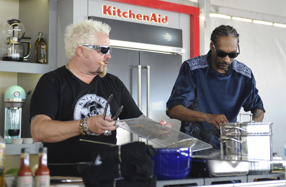 This Feb. 26, 2017 photo made available by WorldRedEye.com, shows rapper Snoop Dog, right, and Chef Guy Fieri, cooking together during a demonstration at the South Beach Wine & Food Festival in Miami Beach, Fla. Rappers Snoop, Action Bronson and Rev Run are ushering the culinary world into an era where shows like ““Martha and Snoop’s Potluck Dinner Party” are a hit and rappers like 2 Chainz drop cookbooks along with their albums. (Ryan Troy/WorldRedEye.com via AP)