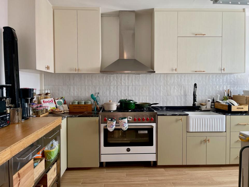 The farmhouse-style kitchen with light green cabinets and a wide oven with a stove top and a large extractor fan.