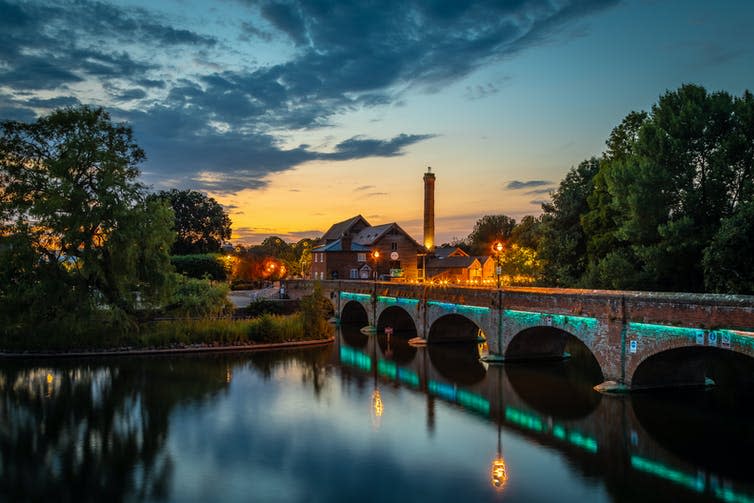 A bridge over a river at dusk with lighted buildings in the background