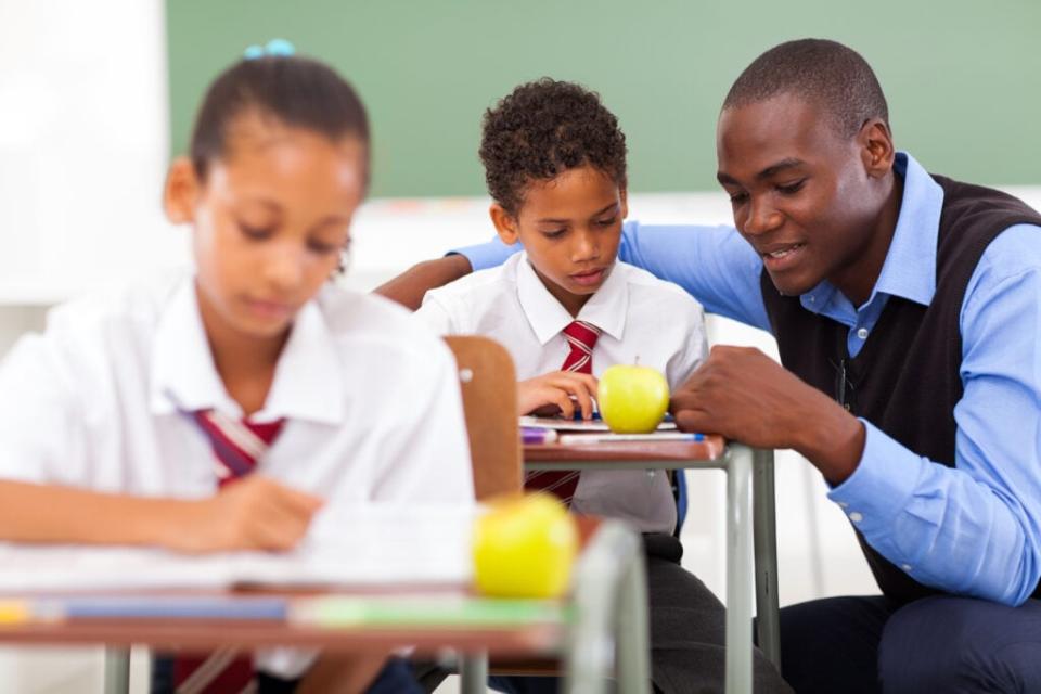 Elementary school teacher helping student in classroom. (Credit: Adobe Stock Image)