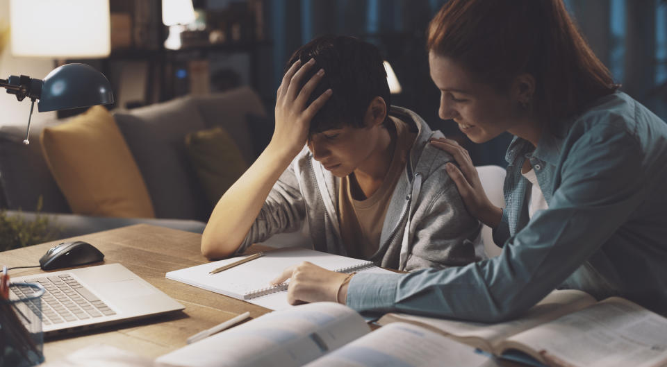 Caring sister helping her younger brother with his homework, he is tired and disappointed