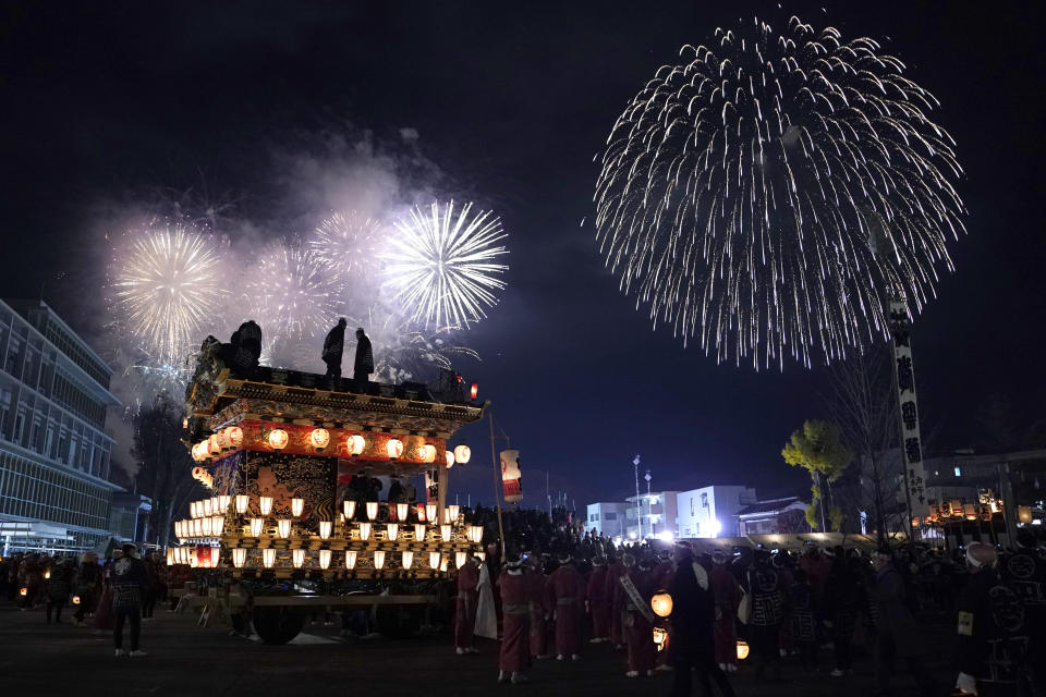 In this Tuesday, Dec. 3, 2019, photo, men stand on top of a lantern-covered float as fireworks light up the sky during the Chichibu Night Festival in Chichibu, north of Tokyo, Japan. Moving six towering floats up a hill and into the town center is the culminating moment of a Shinto festival that has evolved from a harvest thanksgiving into a once-a-year meeting between two local gods. (AP Photo/Toru Hanai)