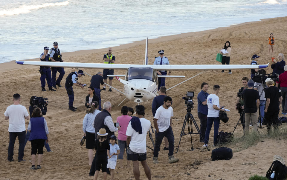 Spectators stand near a light plane that made an emergency landing on a beach in Sydney Wednesday, May 26, 2021. The recreational plane landed safely on a Sydney beach with three people aboard including a baby on Wednesday after its single engine failed, officials said. (AP Photo/Mark Baker)