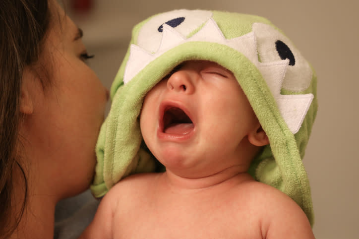 Woman holding a crying baby with a green towel draped over the baby’s head that resembles a monster