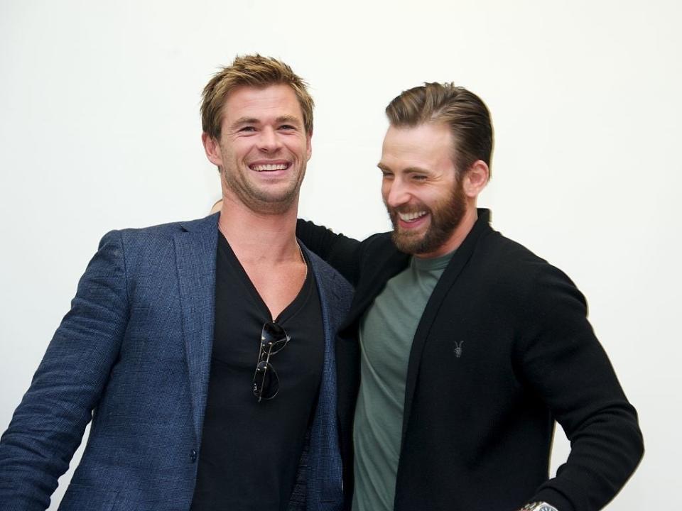 Chris Hemsworth and Chris Evans share a laugh, with Hemsworth in a blazer and V-neck shirt and Evans in a casual jacket and shirt