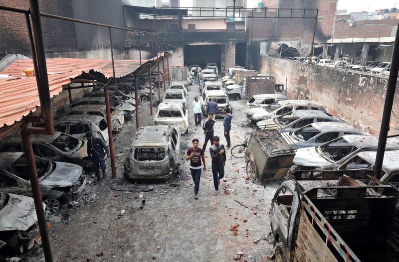 Men look at burnt vehicles at a parking lot in a riot affected area following clashes between people demonstrating for and against a new citizenship law in New Delhi