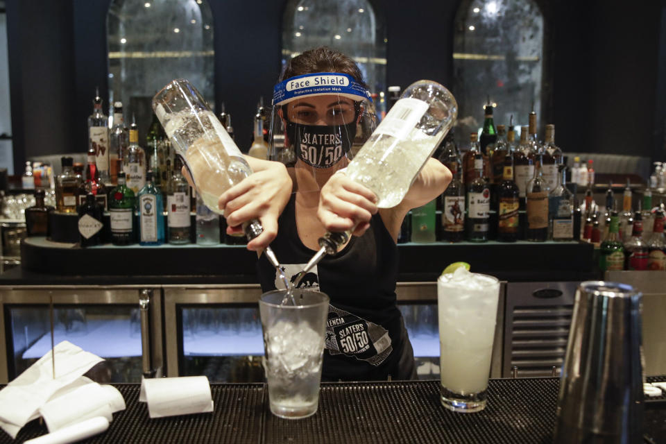 FILE - In this July 1, 2020, file photo, a bartender mixes a drink while wearing a mask and face shield at Slater's 50/50 in Santa Clarita, Calif. Getting children back to school safely could mean keeping high-risk spots like bars and gyms closed. That's the latest thinking from some public health experts. (AP Photo/Marcio Jose Sanchez, File)
