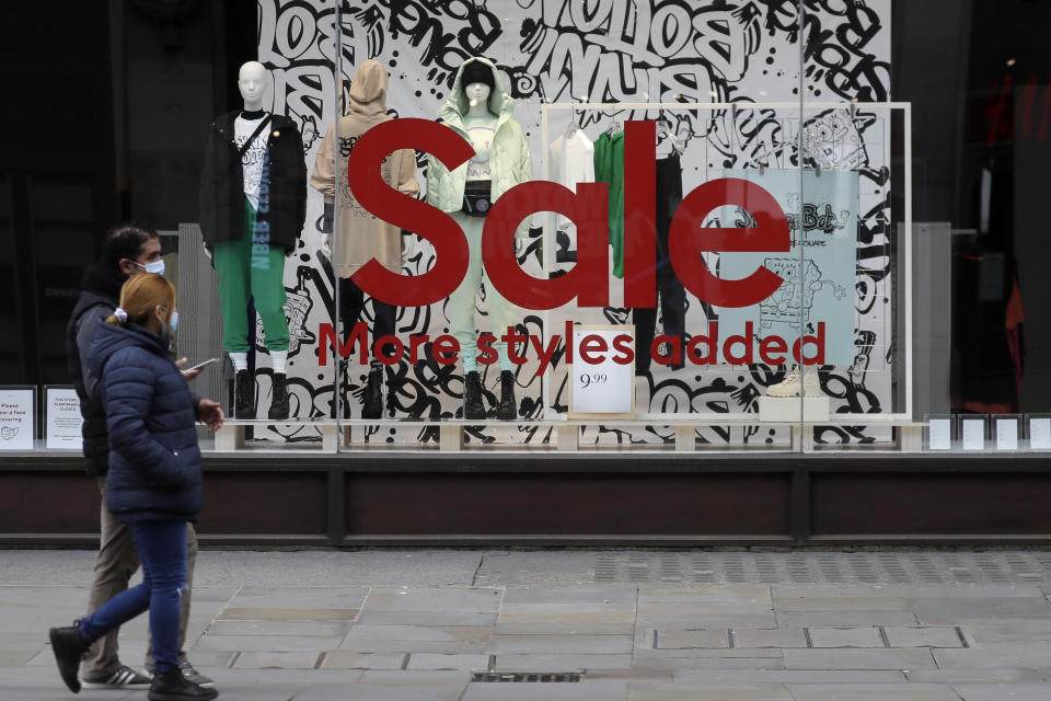 Pedestrians walk past a Sale sign in the window of a closed shop on Oxford Street in London, Saturday, Dec. 26, 2020. London is currently in Tier 4 with all non essential retail closed and people have been asked to stay at home, on what is usually one of the busiest retail days of the year with the traditional Boxing Day sales in shops. (AP Photo/Kirsty Wigglesworth)